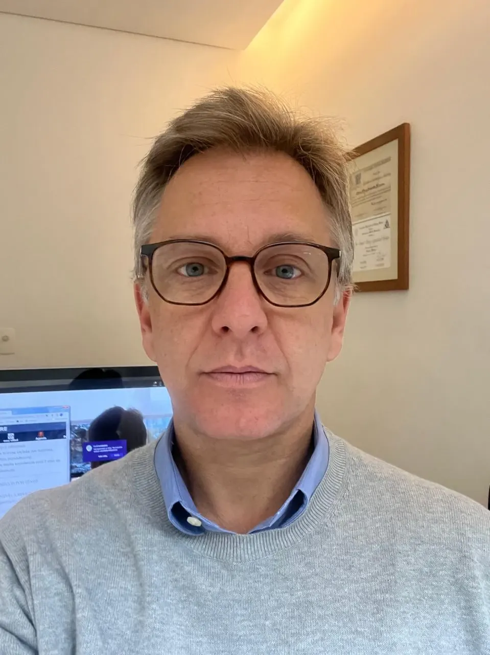 Dr. Daniel Lerario em seu consultório, com diplomas ao fundo